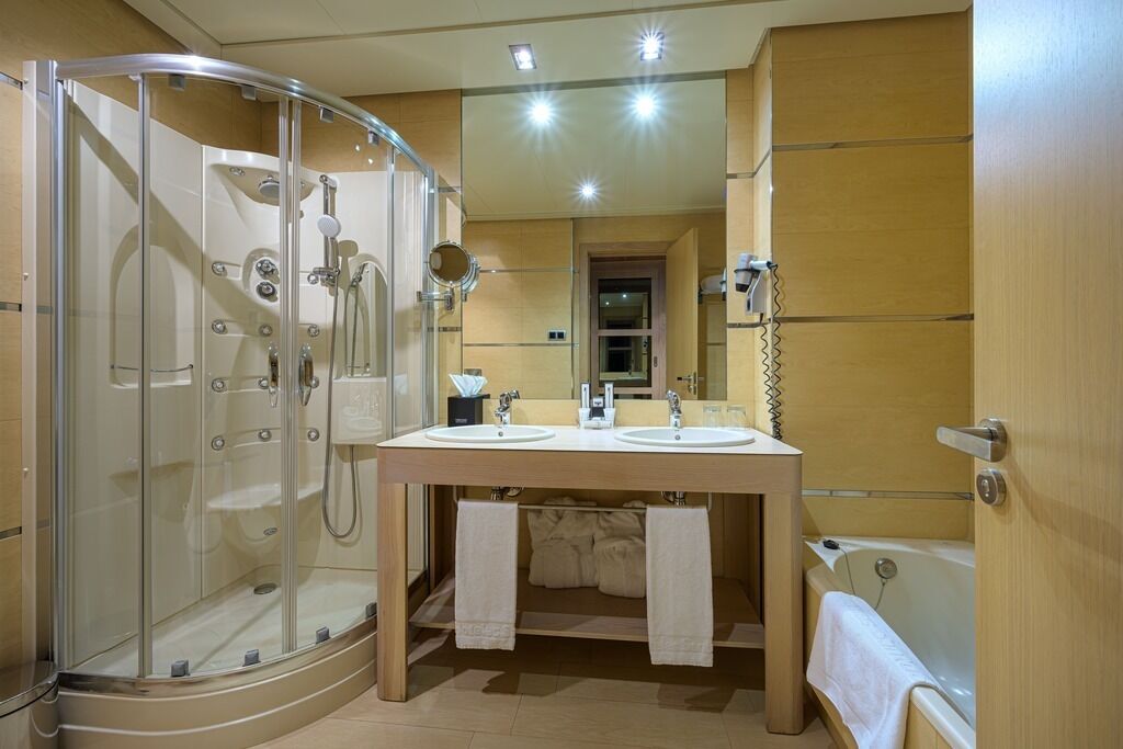 A bathroom with a glass-enclosed shower, two sinks, a bathtub, and a mirror above the sinks.