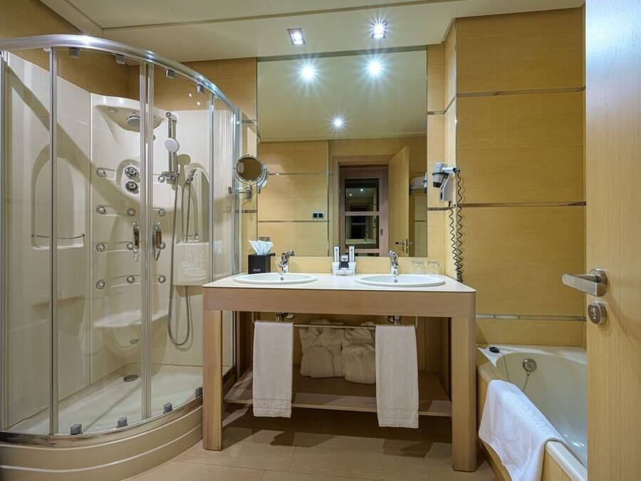 A bathroom with a glass-enclosed shower, two sinks, a bathtub, and a mirror above the sinks.