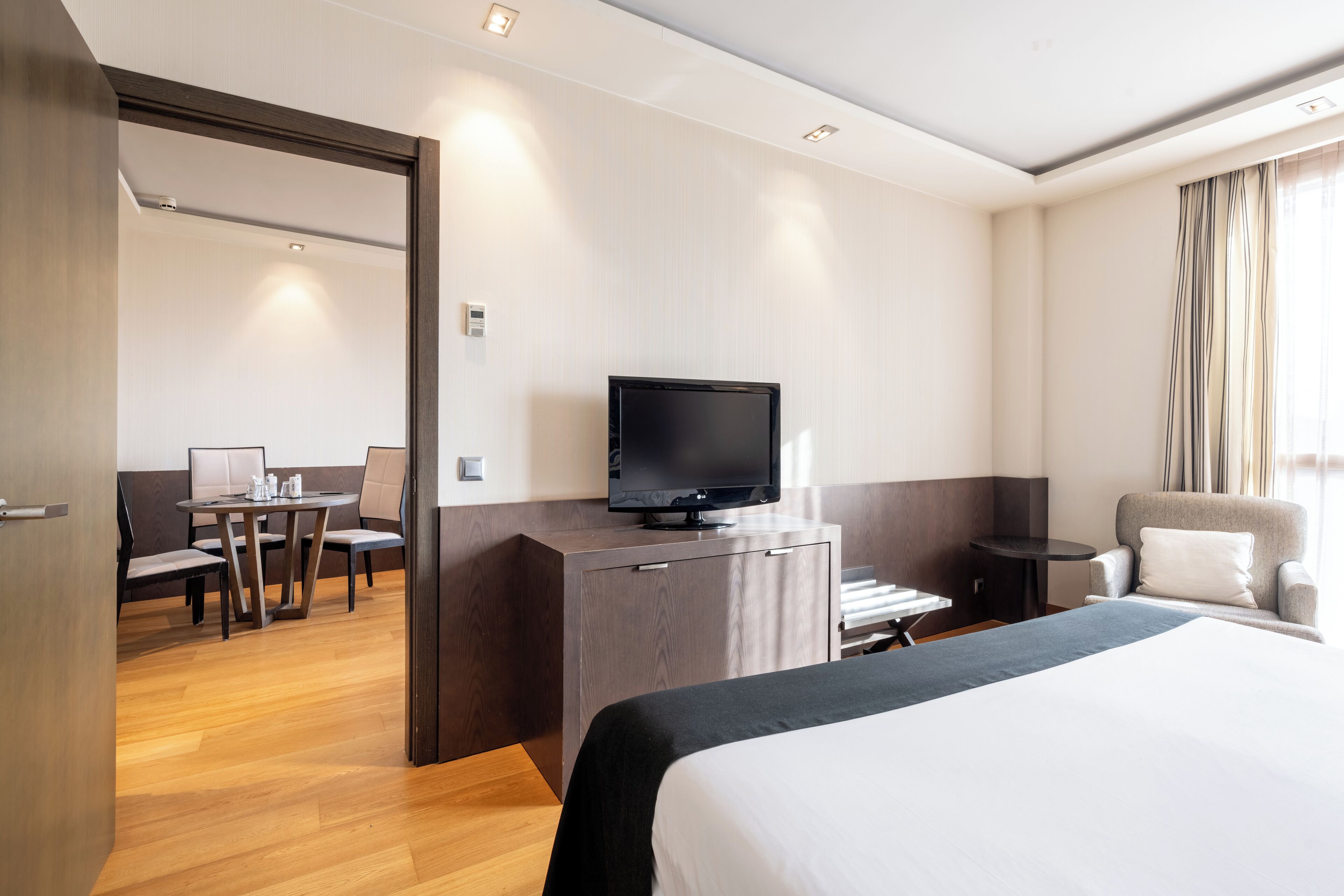 A hotel room with a bed, a TV, a desk with a chair, and a small table.