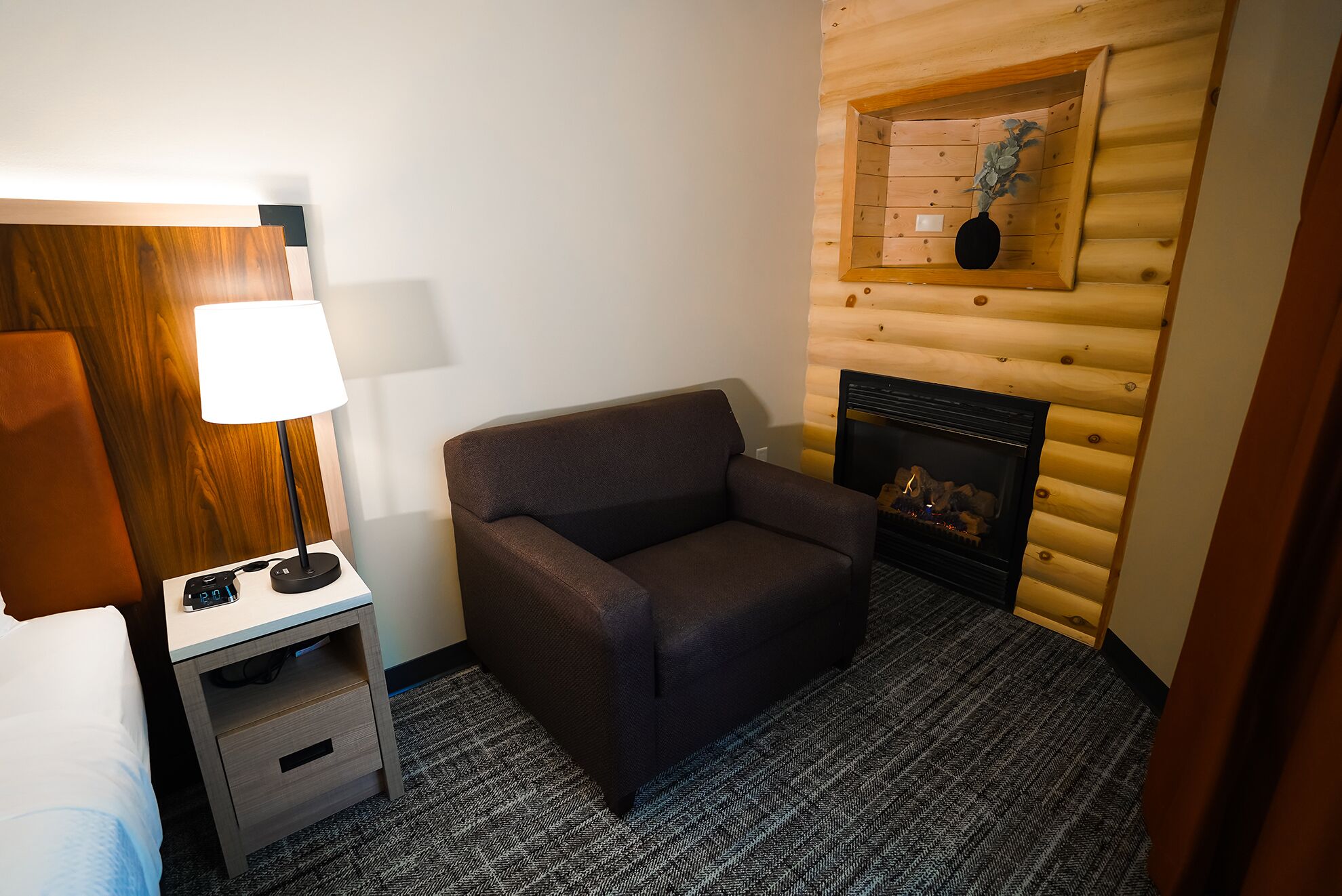 Habitación de hotel con pared de madera, chimenea, sofá, escritorio con lámpara y cama.