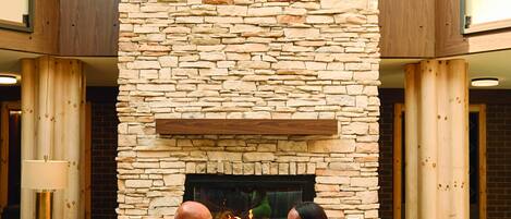 A stone fireplace with a fire, a seating area with a sofa and armchairs, and a high ceiling with skylights.