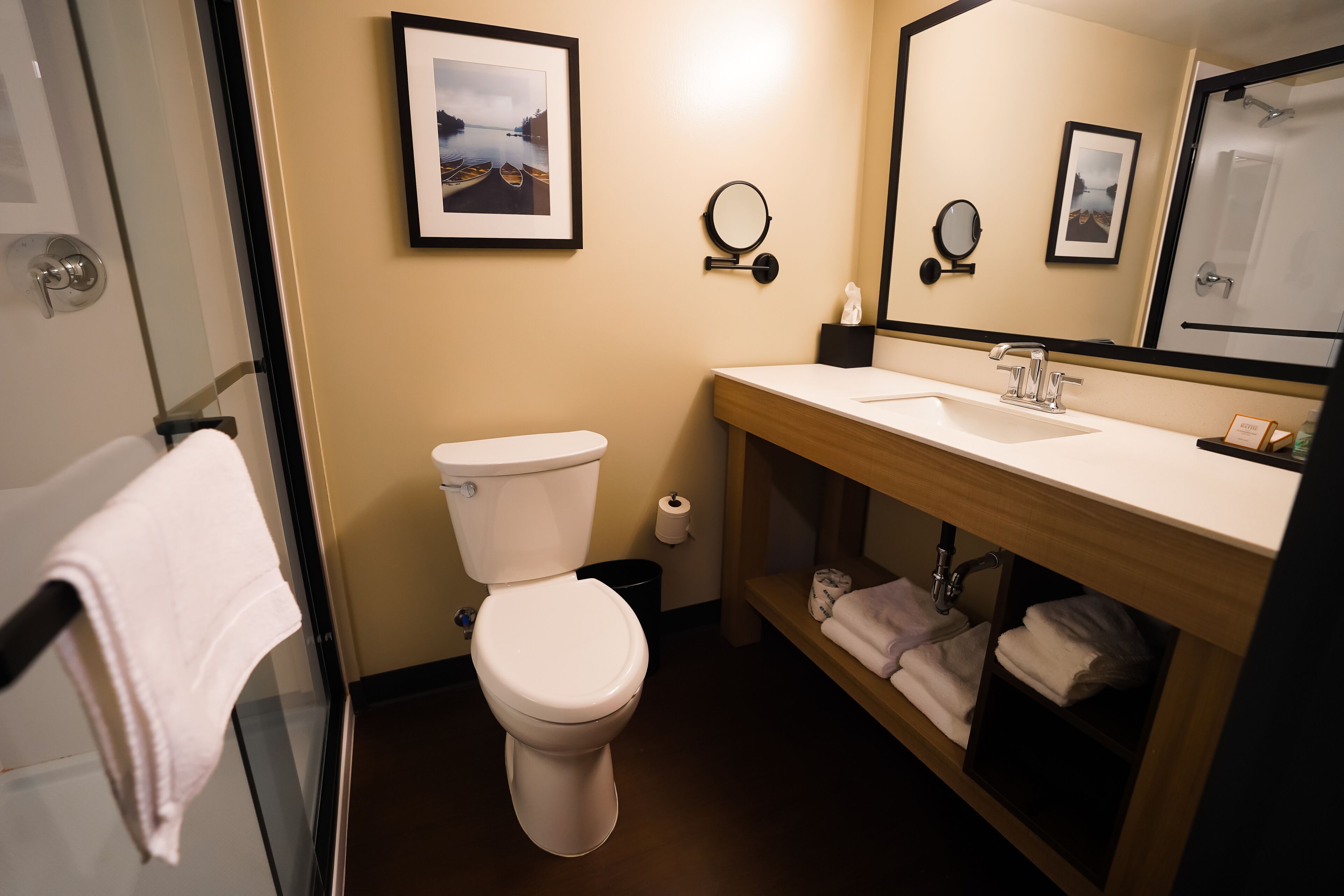 Et moderne badeværelse med toilet, vask og bruser. Væggene er dekoreret med billeder i rammer, og der er en håndklædestang.