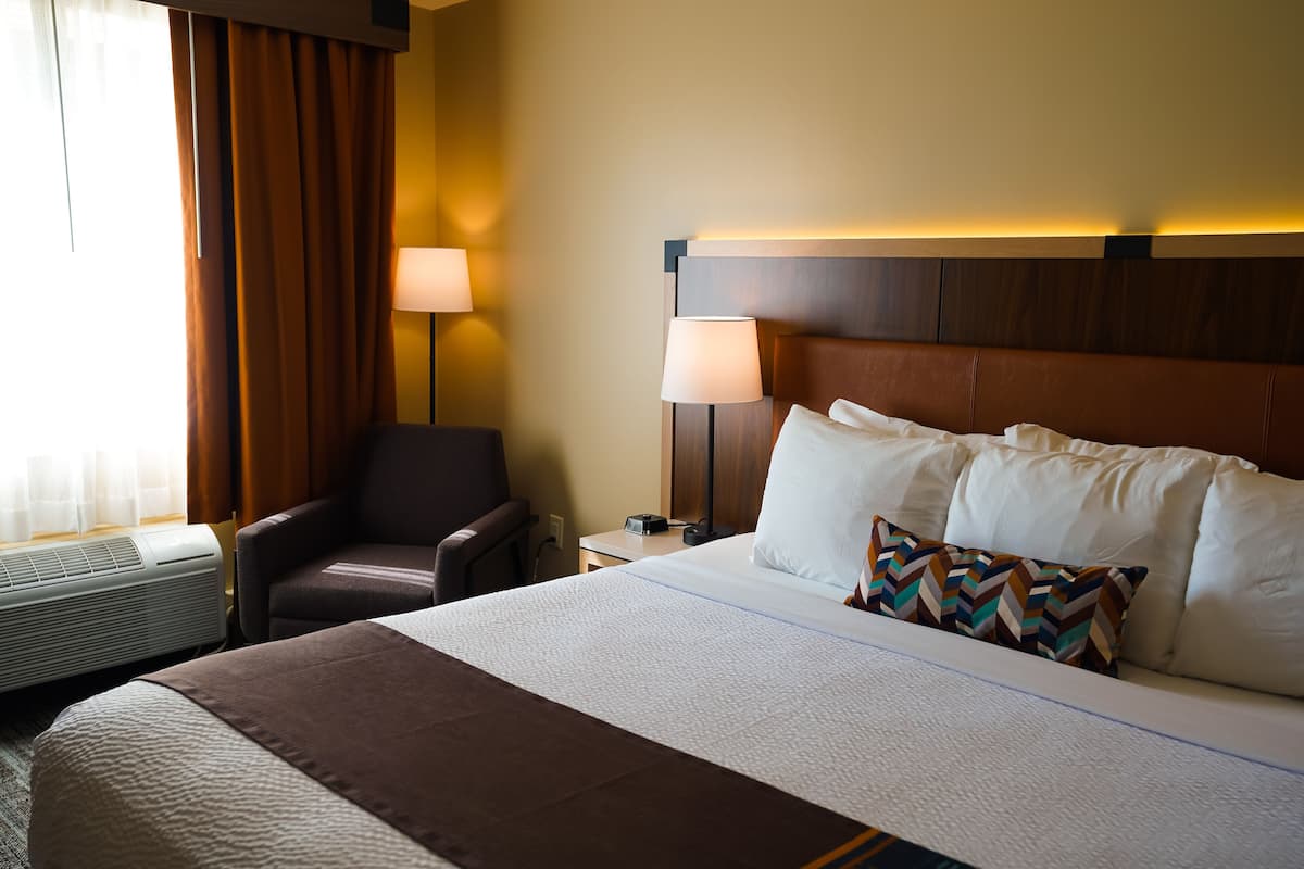Une chambre d’hôtel avec un grand lit, deux lampes de chevet, une chaise et une fenêtre avec des rideaux.