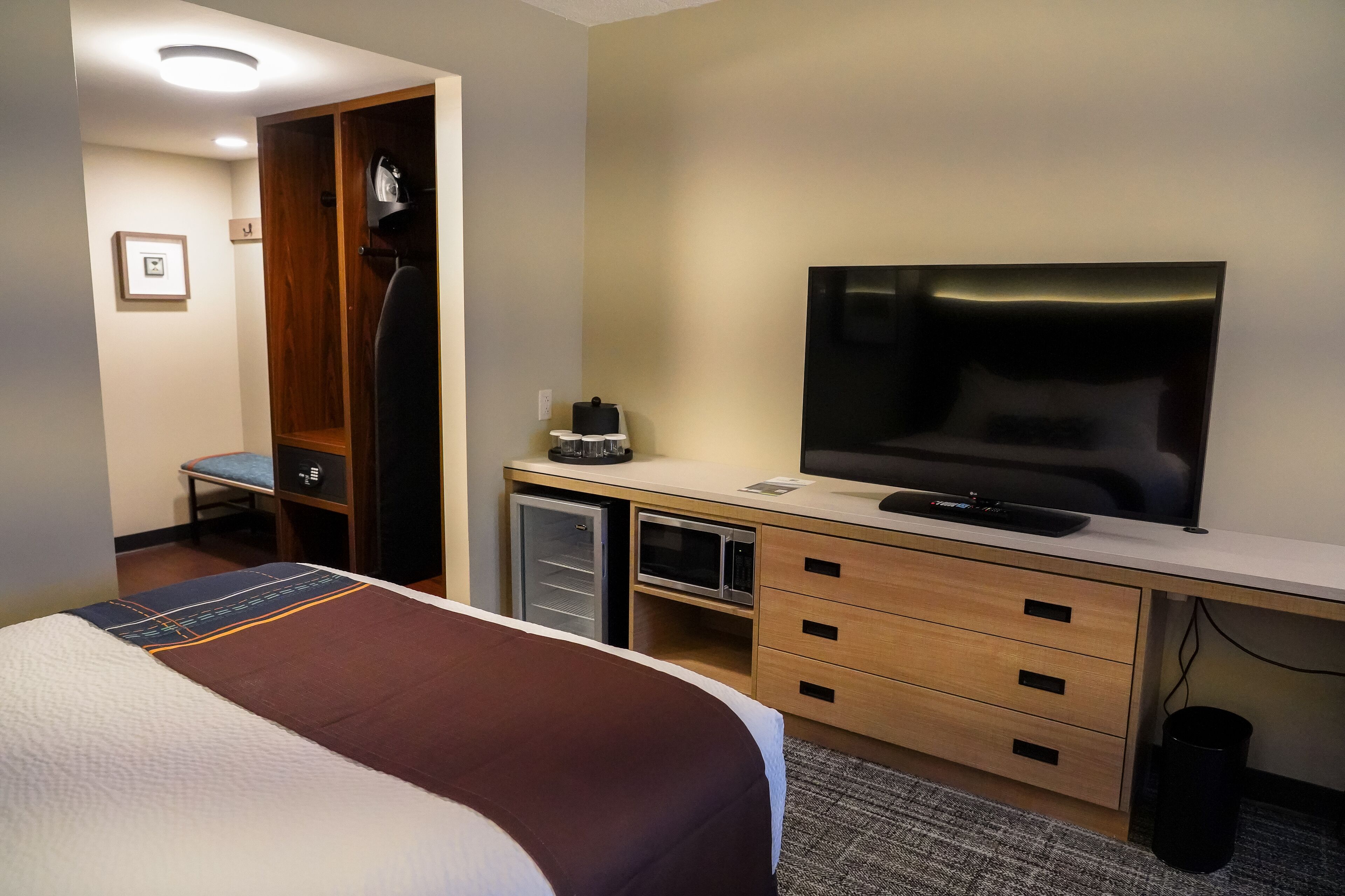 A hotel room with a bed, a TV, a desk with drawers, a microwave, and a small refrigerator.