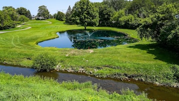 A golf course with a pond, a small stream, and a house in the background.