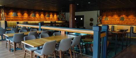 A modern restaurant with wooden tables and chairs, a long counter, and a brick wall with hanging lights.