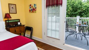 Ein Hotelzimmer mit Bett, Schreibtisch, Stuhl, einem Fenster mit Jalousien und einem Balkon mit Sitzgelegenheit.