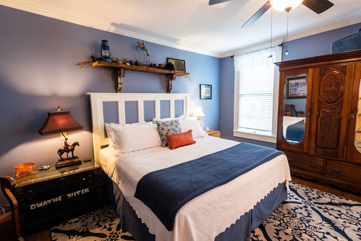A bedroom with a bed, nightstands, a dresser, and a window with blinds.