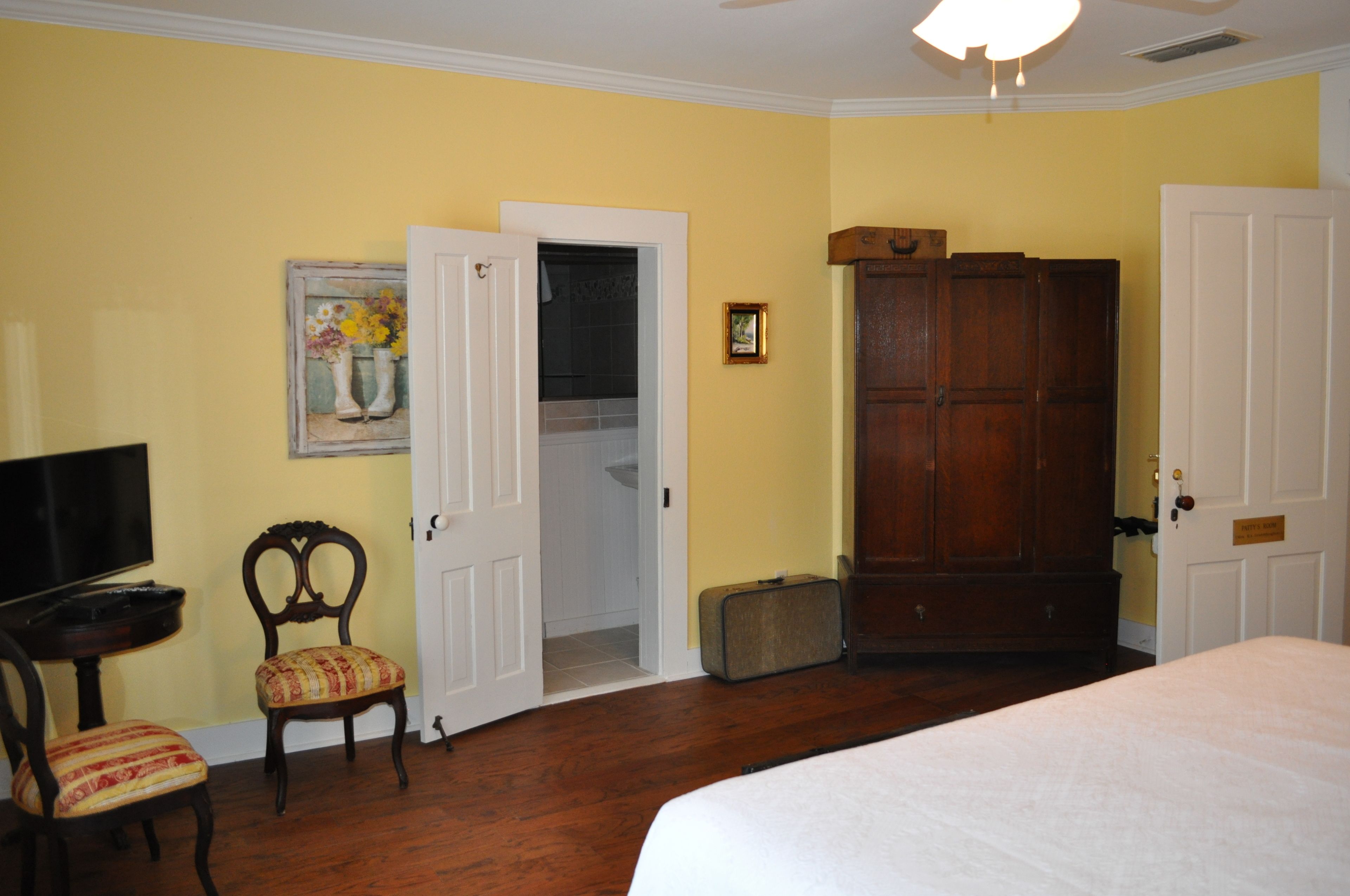 A room with a bed, a television, a chair, a wardrobe, and a door leading to a bathroom.