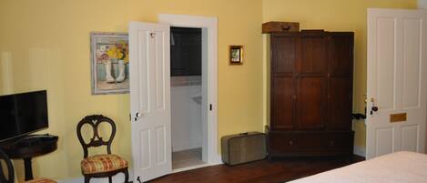 A room with a bed, a television, a chair, a wardrobe, and a door leading to a bathroom.
