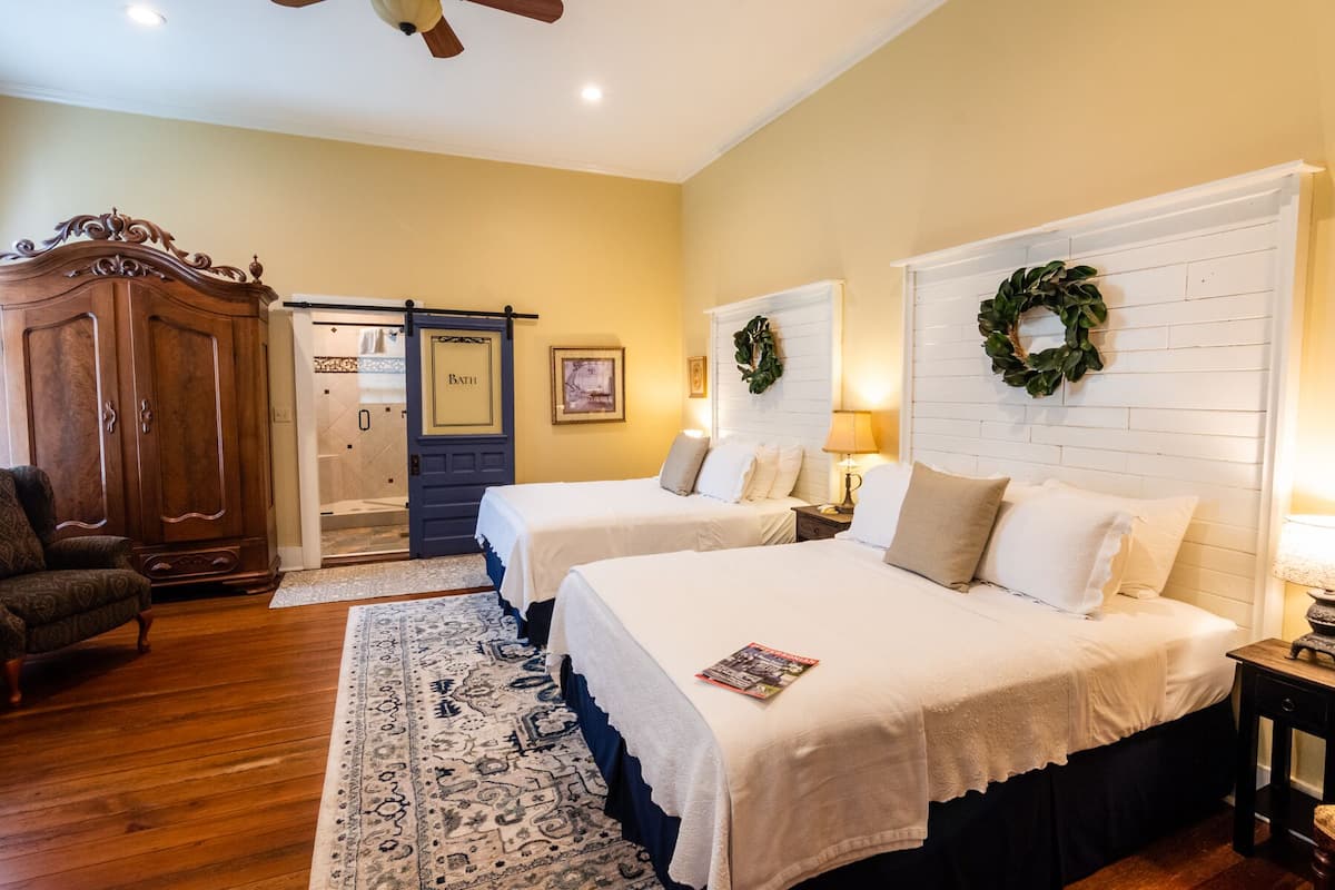 A bedroom with two beds, a wooden wardrobe, a bathroom door, and a patterned rug.