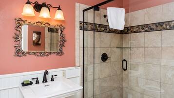 A bathroom with a white sink, ornate mirror, and a shower with a stone tile border.