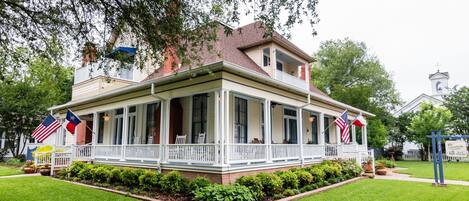 A two-story house with a porch, surrounded by well-maintained lawn and trees.