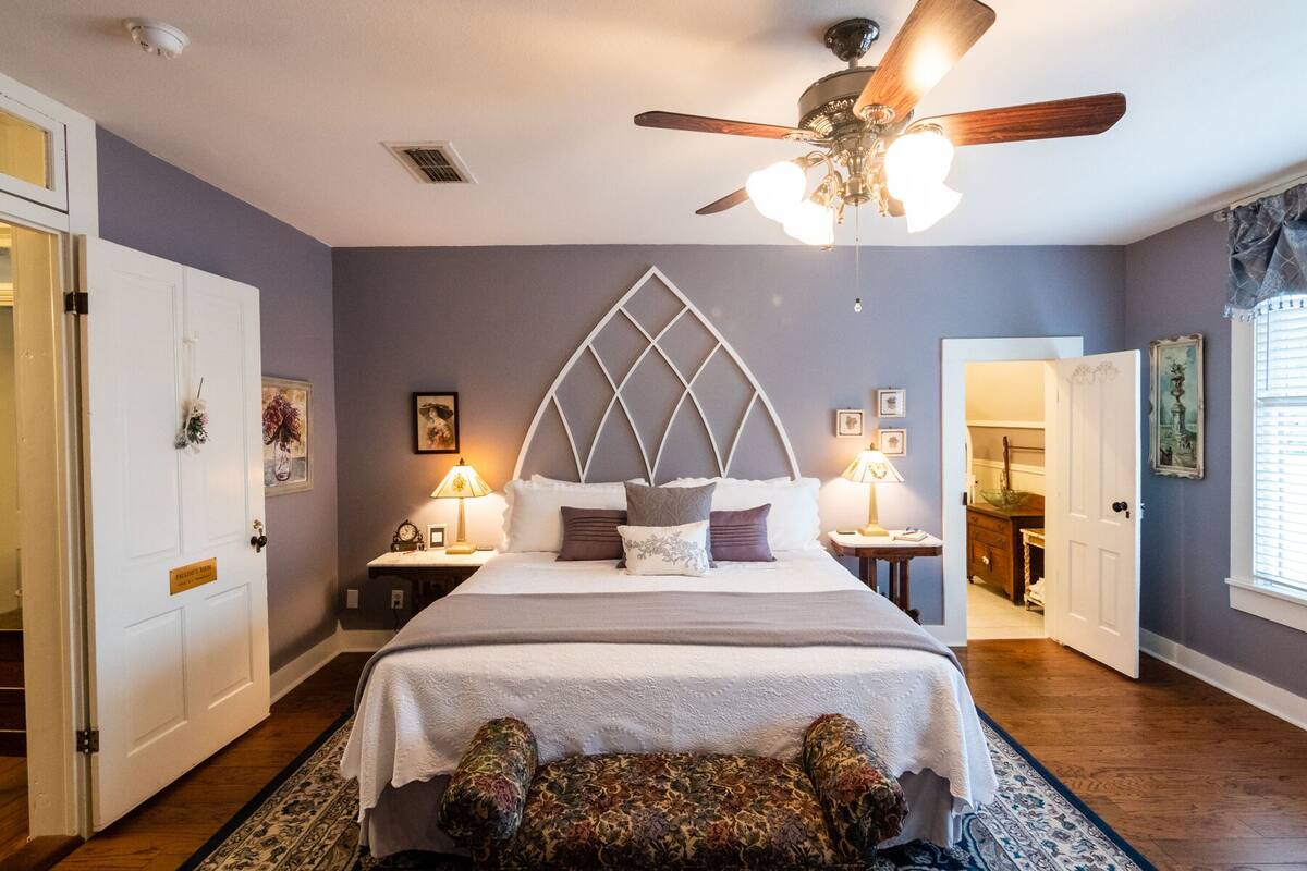 A bedroom with a bed, a ceiling fan, a nightstand, a dresser, and a door.
