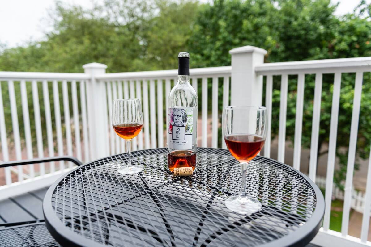 A metal table with a bottle of Jefferson Select wine and two glasses on a balcony with a white railing.