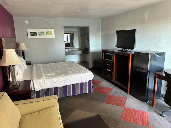 Une chambre d’hôtel comprenant un lit, un bureau avec une télévision, un réfrigérateur, un miroir et une petite kitchenette.