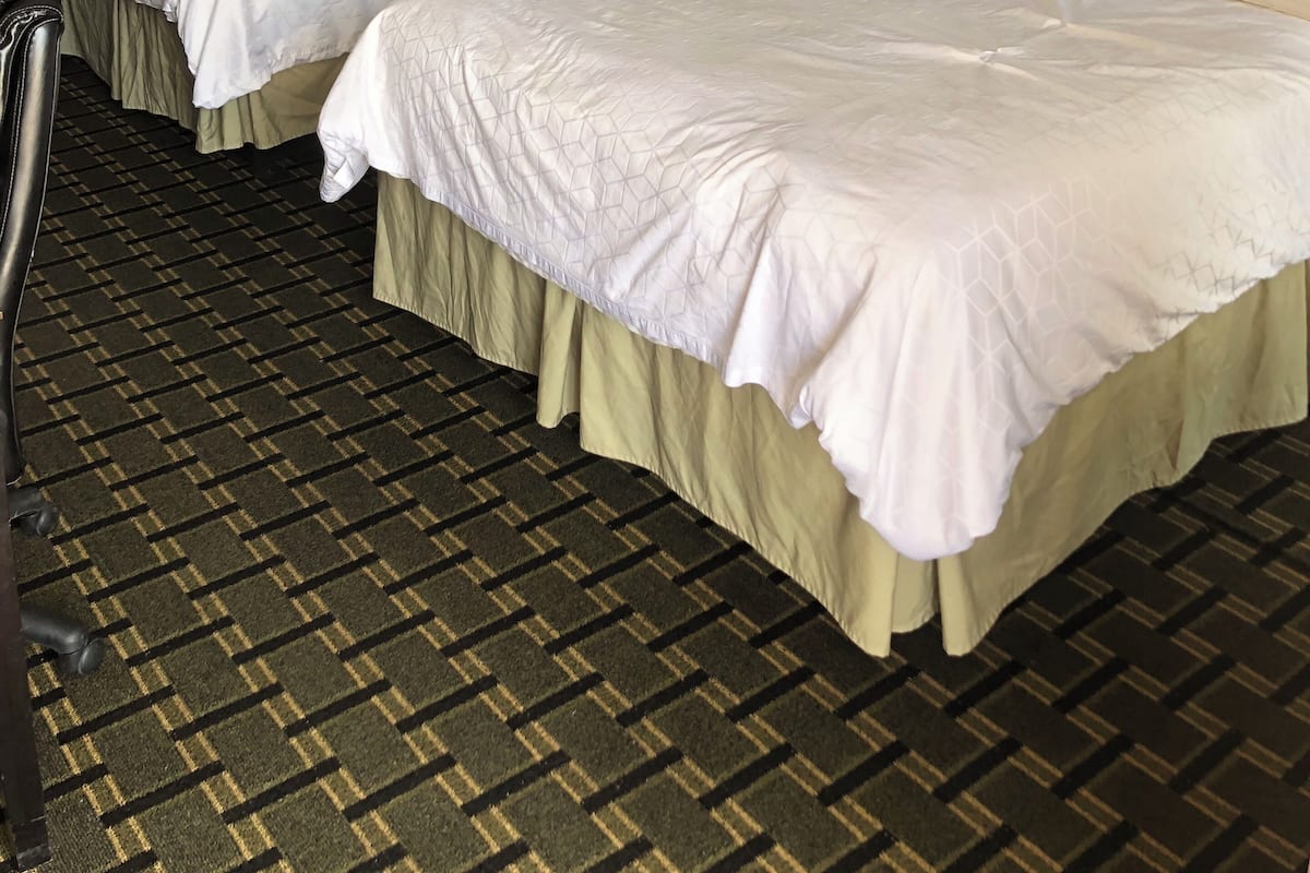 Habitación de hotel con dos camas, cabecero, lámpara de pared y alfombra estampada.