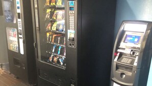 A row of vending machines and a small ATM in a hallway with wooden flooring. - Executive Inn (Edmond)