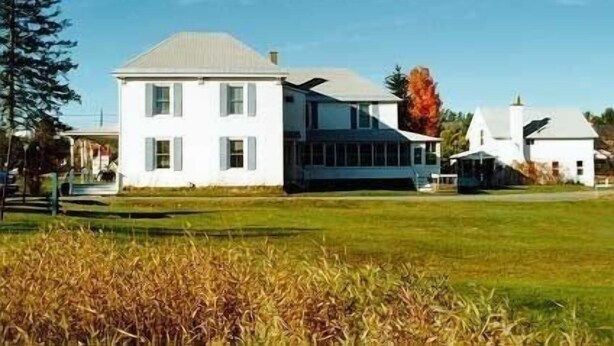 A two-story white house with a large front porch and a smaller attached structure.