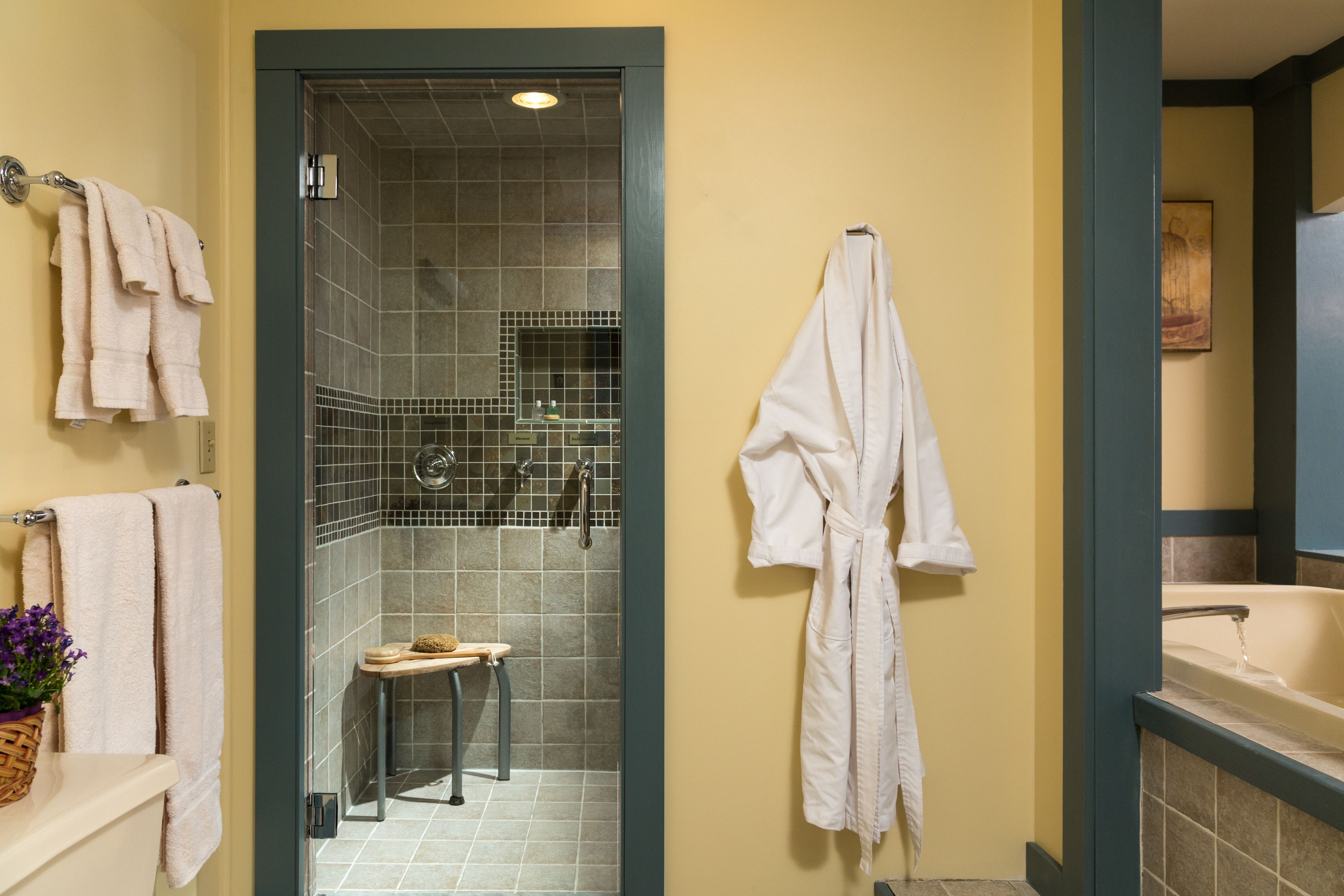 A bathroom with a shower, a bathtub, and a toilet. There are towels hanging on the wall and a bath mat on the floor.