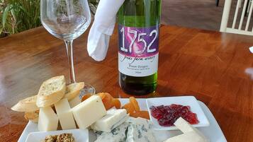 A table with a bottle of wine, a glass, and a cheese board with various cheeses and fruits.