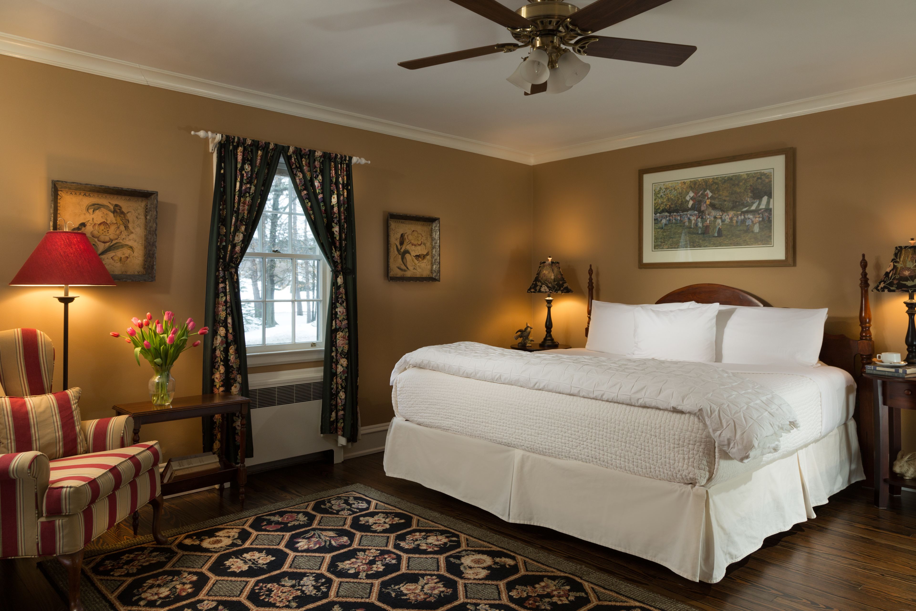 A bedroom with a large bed, a chair, a table with a lamp, and a window with curtains.
