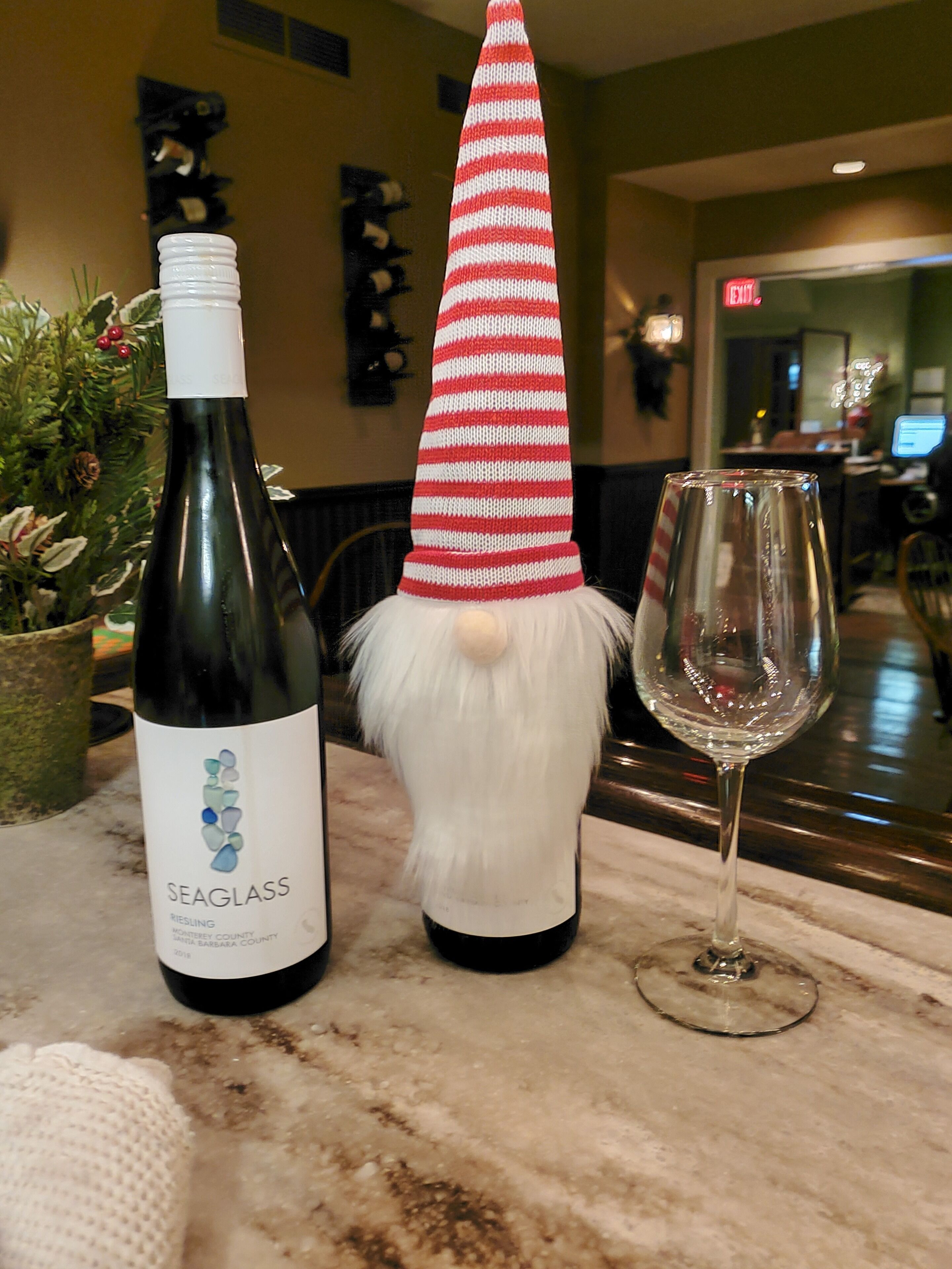Una botella de vino Riesling Seaglass, una figura de gnomo con sombrero a rayas rojas y blancas, y una copa de vino vacía sobre una encimera de mármol.