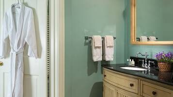 A bathroom with a sink, mirror, towels, and a robe hanging on a door.