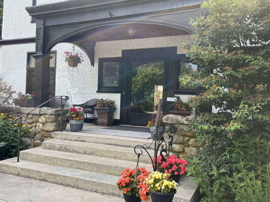 A building with a stone staircase leading to a black door, surrounded by potted plants and a stone wall.