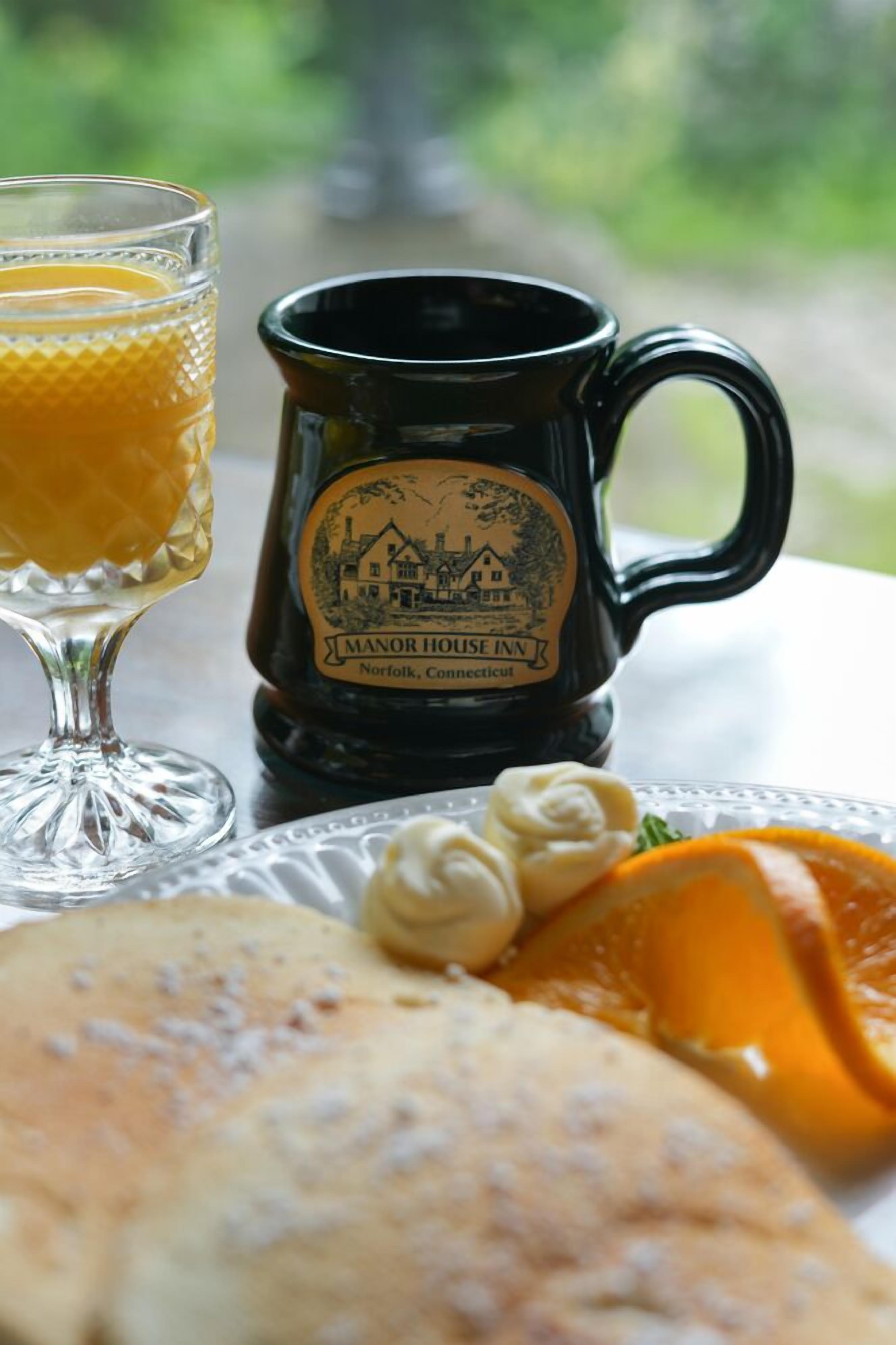 Un vaso de jugo de naranja, una taza negra con una etiqueta y un plato con alimentos.