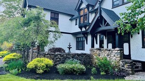 A large, two-story house with a steeply pitched roof, stone foundation, and a well-maintained garden with various shrubs and a fountain. - Manor House Inn (Norfolk)