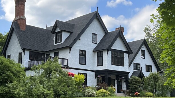 A large, two-story house with a steeply pitched roof, multiple chimneys, and a well-maintained lawn.