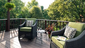 A covered outdoor deck with wicker furniture, a small table with drinks, and a potted plant.