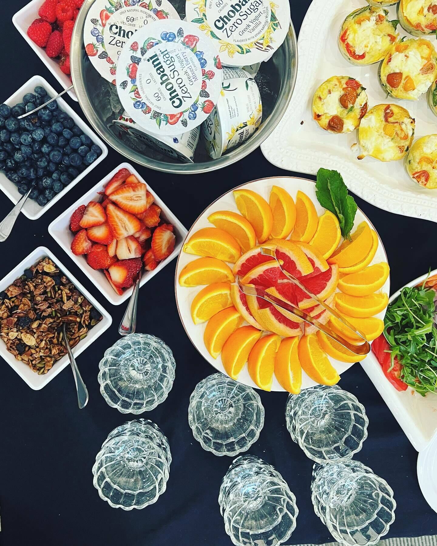A table with various food items including yogurt cups, strawberries, blueberries, granola, and a fruit platter.
