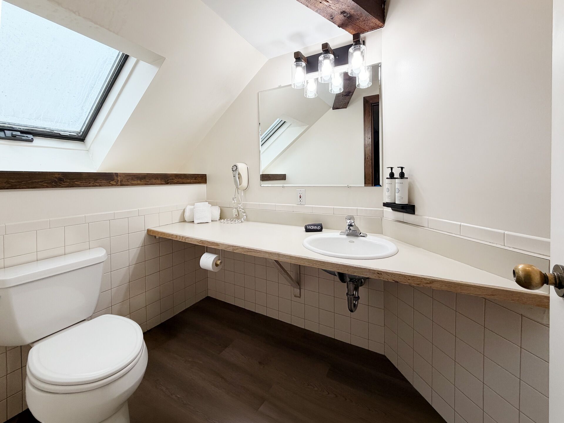 Un baño con tragaluz, inodoro, lavabo y espejo.