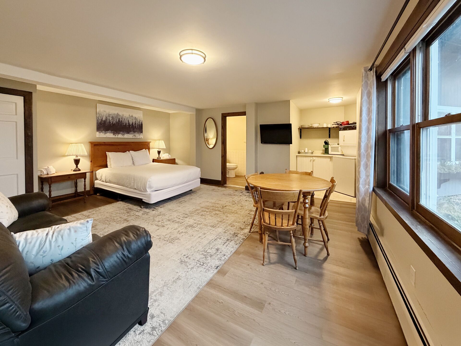Una habitación de hotel con cama, sofá, mesa de comedor con sillas, televisión y ventana.