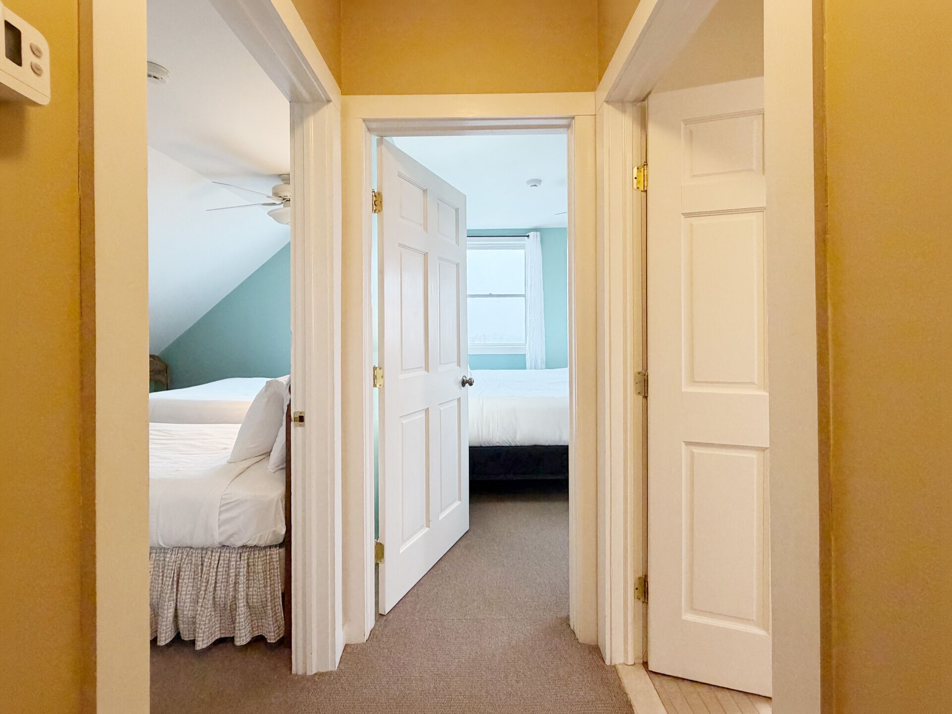 A hallway leading to a bedroom with a bed, a door, and a ceiling light fixture.