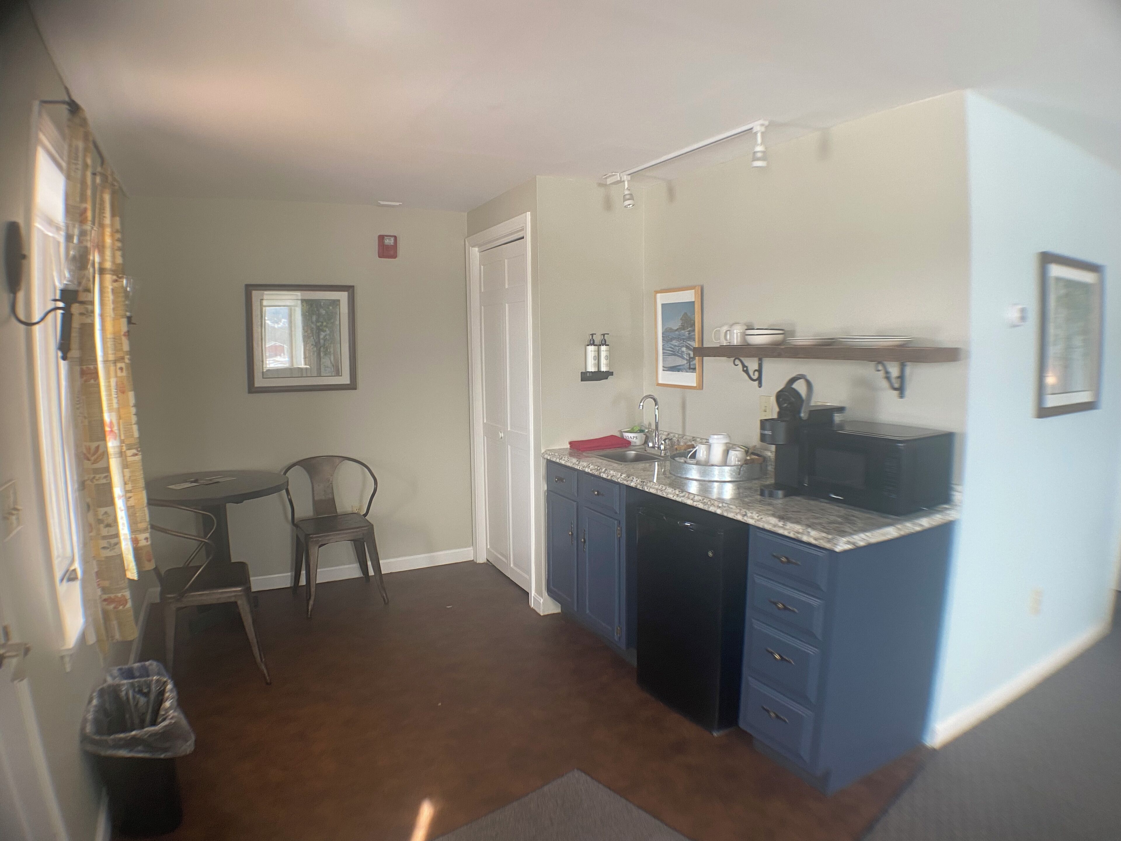 Cocina compacta con lavamanos, cafetera y microondas. En la zona de comedor contigua hay una silla y una mesa pequeña.
