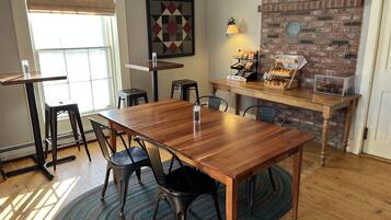 Un coin repas avec une table en bois, des chaises noires, un tapis à motifs, un mur en briques et une fenêtre avec des stores.