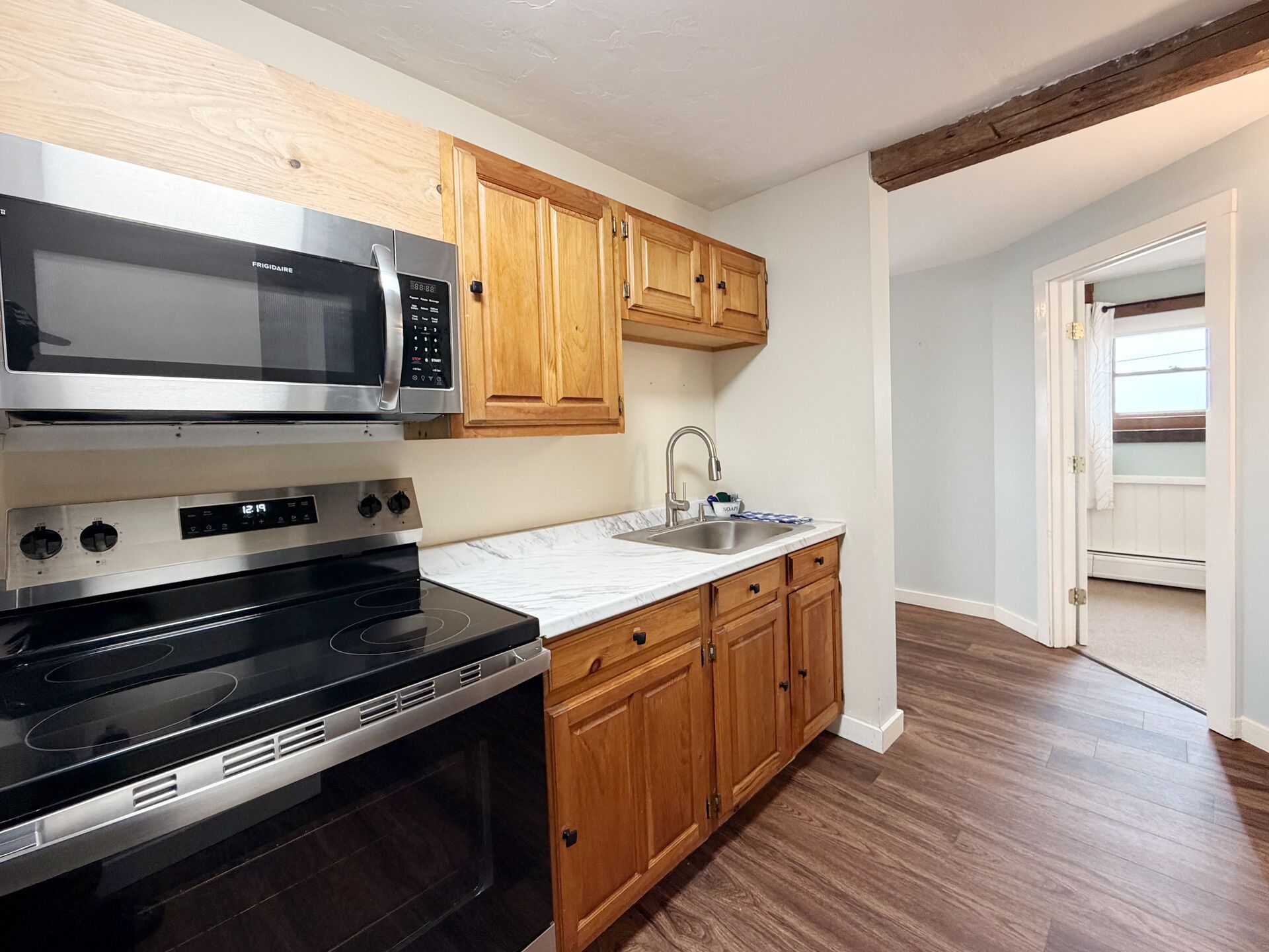 A kitchen with wooden cabinets, a stainless steel microwave, a stove, and a sink.