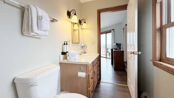 A bathroom with a toilet, sink, and mirror. There is a towel rack with towels, a wooden cabinet, and a door leading to another room.