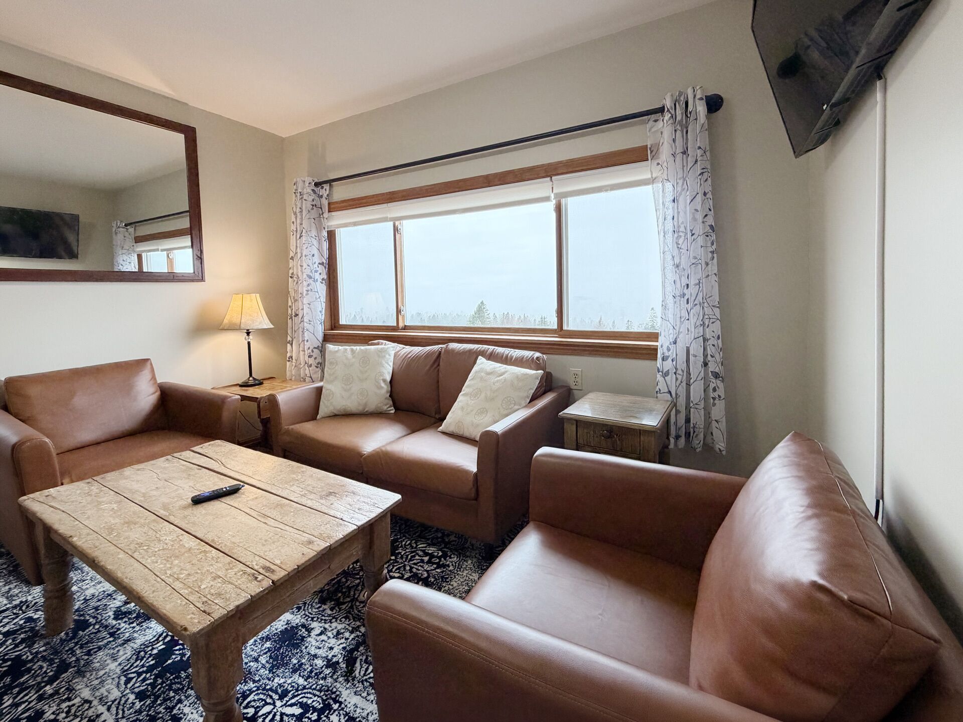 A living room with a sofa, a coffee table, a TV, and a window with curtains.