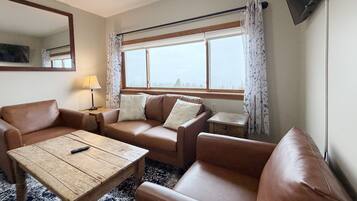A living room with a sofa, a coffee table, a TV, and a window with curtains.