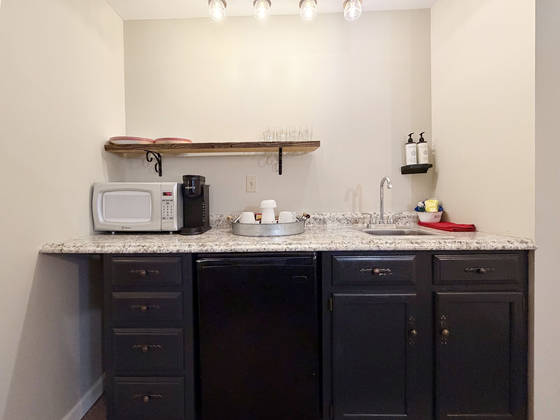 Una cocina con microondas, cafetera, lavabo y armarios.
