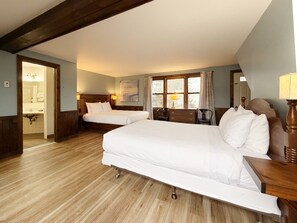 A hotel room with two beds, a wooden floor, a window with curtains, a desk with a lamp, and a mirror. - The Wildflower Inn (Lyndonville)