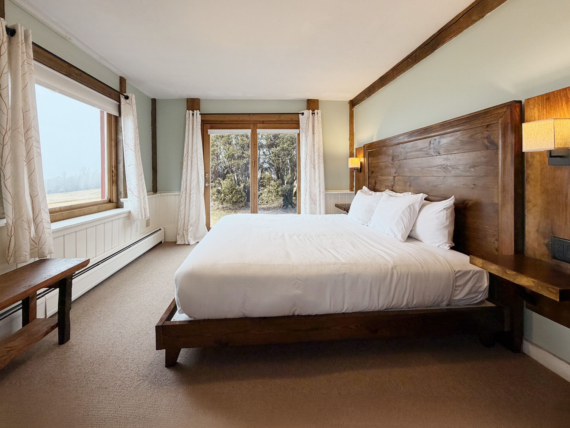 Un dormitorio con cabecera de madera, una cama grande, un banco y una ventana con cortinas.
