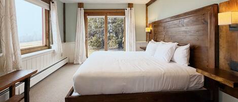 Un dormitorio con cabecera de madera, una cama grande, un banco y una ventana con cortinas.