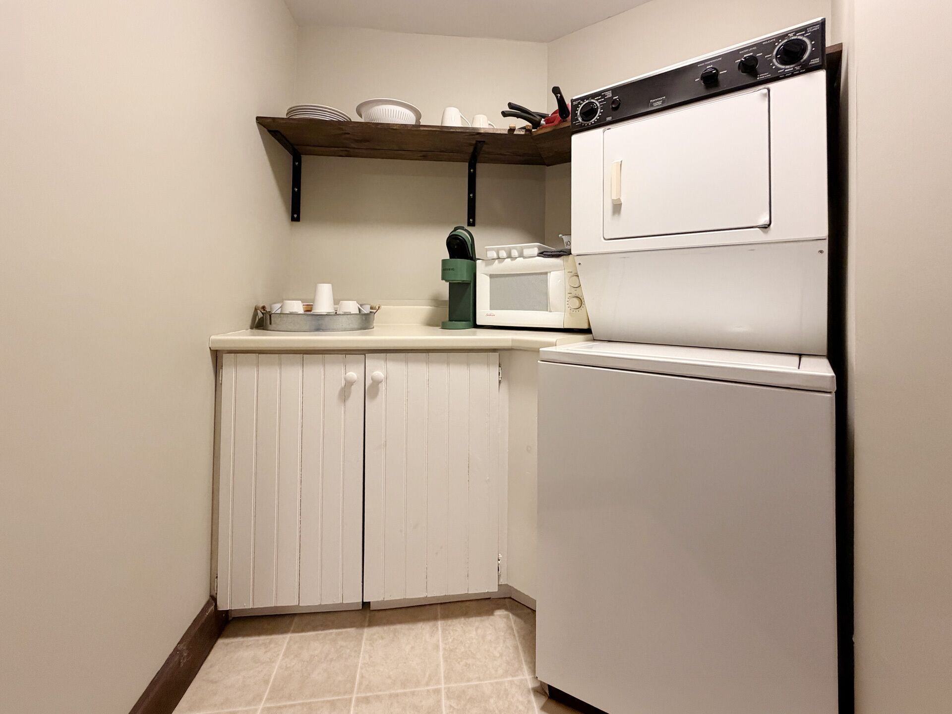 Una cocina compacta con microondas, un refrigerador blanco y un estante de madera sobre los gabinetes.