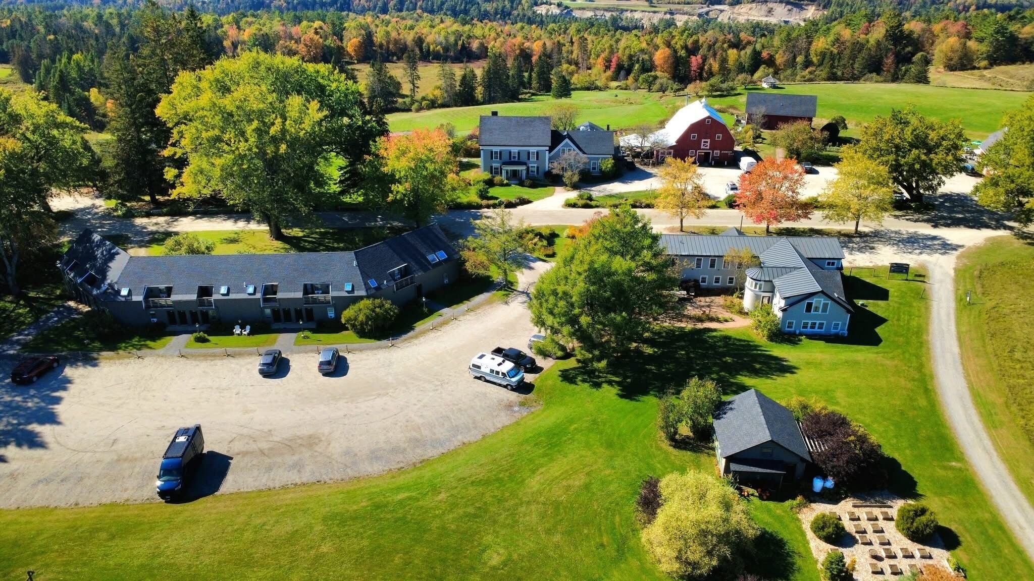 An aerial view of a residential area with multiple houses, a large parking area, and surrounding greenery.