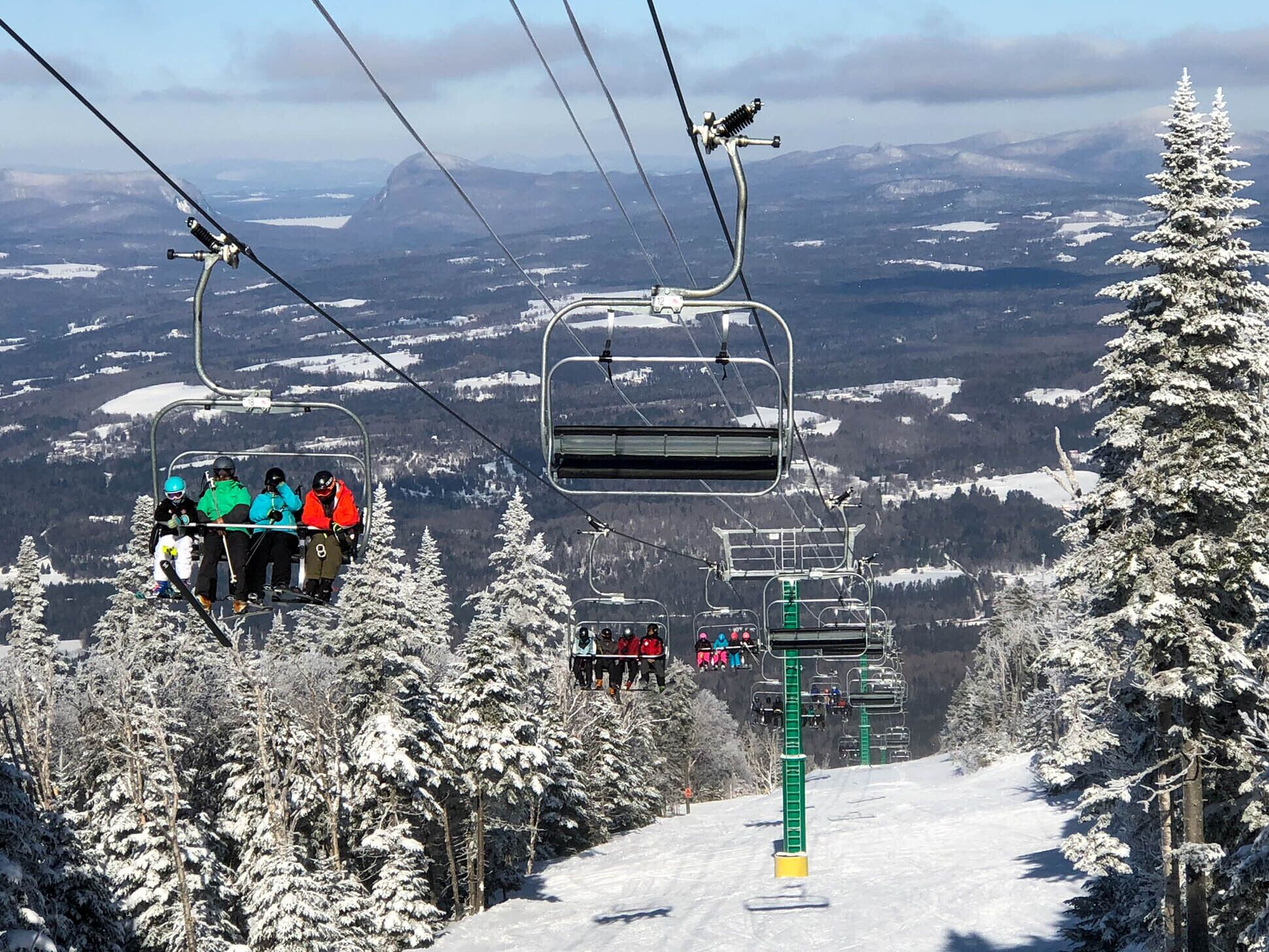 A ski lift with passengers, surrounded by snow-covered trees and a mountainous landscape.